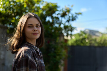 Naklejka premium Smiling woman in a plaid shirt outdoors in a sunny garden. A lifestyle portrait focused on casual style, nature, well being, and confident mood under warm daylight