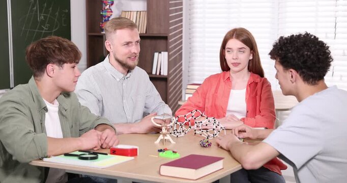 Teacher explaining physics to students at wooden desk in classroom