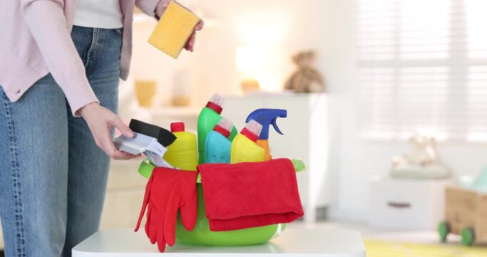 Woman putting squeegee and sponge into plastic basin with cleaning products indoors, closeup