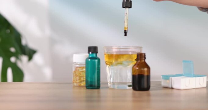 Woman dripping iodine into glass of water from pipette at wooden table, closeup