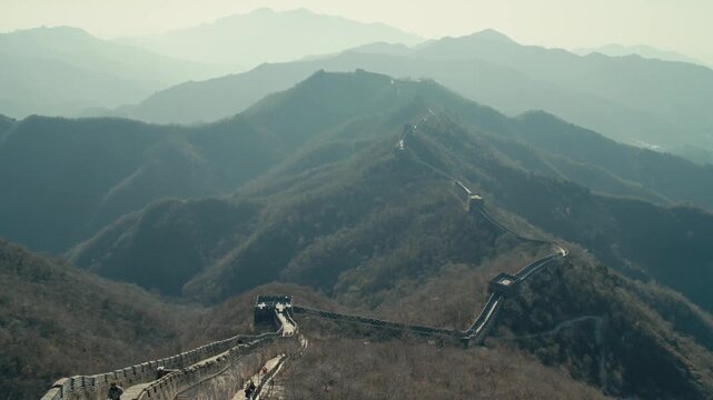 Beijing Ancient Great Wall fortification with stone watchtowers snaking along hazy mountain ridges under soft daylight