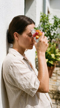 Woman cooling her forehead with an ice-cold fruit infused water glass on a hot summer day