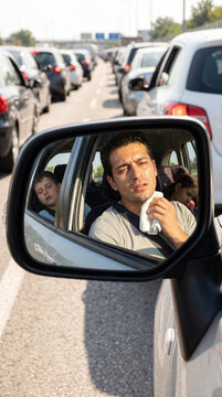Exhausted man wiping sweat during traffic jam reflected in car side mirror with sleeping kids