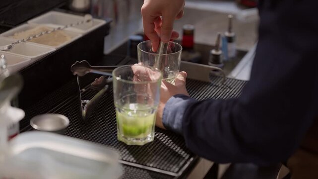 Close up of a bartenders hands using a muddler to crush fresh lime and mint in a glass, preparing a mojito at a stylish bar. Perfect for hospitality and lifestyle content.
