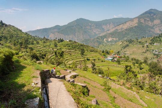 Aerial view of terraced fields and mountain slopes surrounding the Shree Rudranath Temple Gopeshwar, with a person on a stone path in Gopeshwar, Uttarakhand, India.
