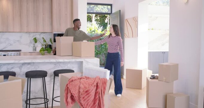 Couple entering open front door holding boxes, placing on marble island, embracing while moving in