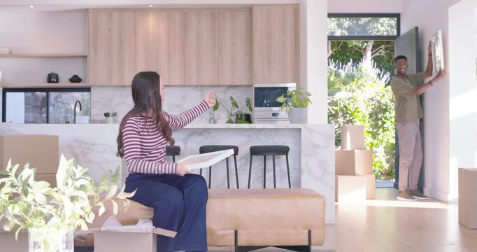 Diverse couple unpacking framed pictures and decorating after moving into open-plan living area