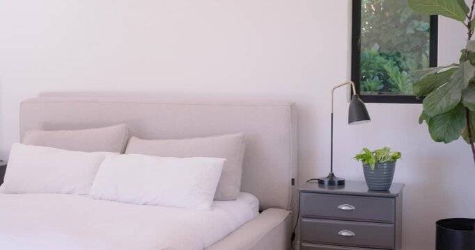 Camera is starting pan left from window revealing bed, duvet, pillows and lamps to showcase styling