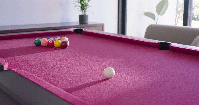 White cue ball is rolling slowly across magenta felt pool table toward racked balls after strike