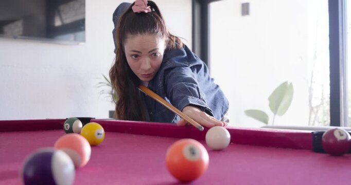 Adult woman approaching pool table at home, aiming, striking cue ball, holding cue smiling for fun