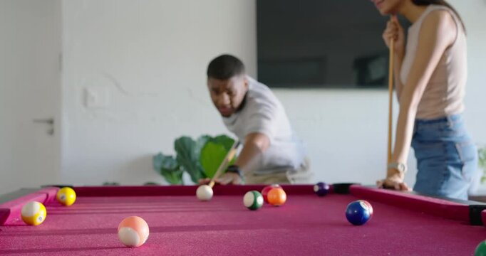 African American couple playing pool at home on magenta table, man striking cue ball after stepping