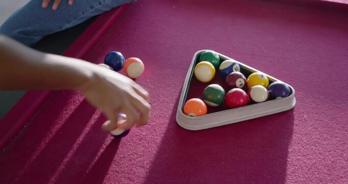 African American couple taking green ball, racking numbered balls at magenta table for break