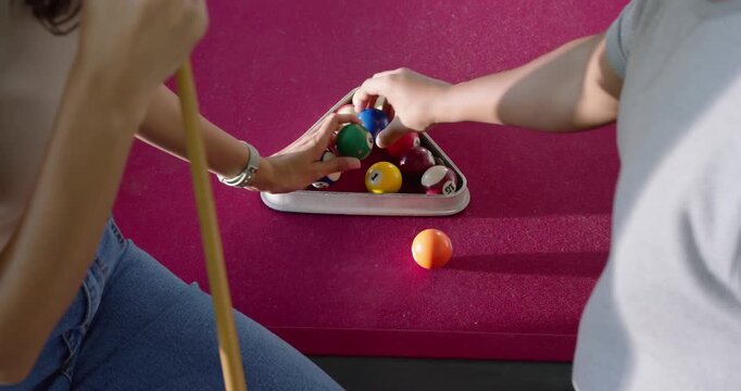 African American couple picking up loose billiard balls and tightening rack on magenta pool table