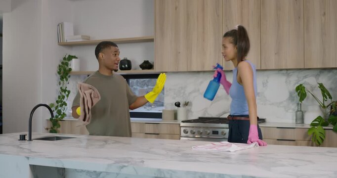 African American couple donning gloves, wiping marble kitchen island, miming blue spray, cleaning