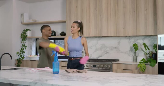 African American couple at kitchen island using spray cleaning counter tugging gloves and laughing