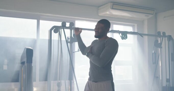 African man in grey top pulling, swinging arms, preparing for workout in gym, cable machine