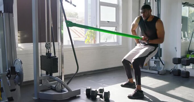 Mid-adult man in tank top sensing tension, pulling band at gym cable, building strength, copy space