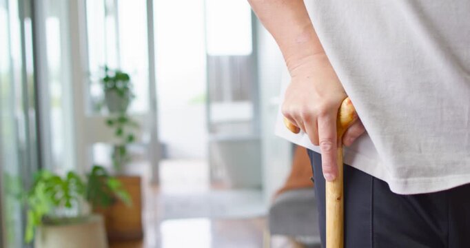 Senior Asian man adjusting wooden cane and tucking tissue for stability in living room, copy space