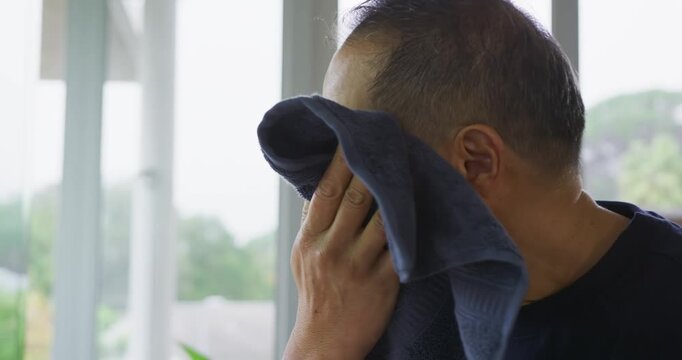 Senior Asian man lifting dark blue towel, wiping, patting face to dry on porch, copy space