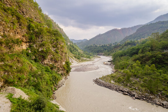 Aerial view of the Alaknanda River flowing through the mountainous landscape of the Himalayas with lush green slopes and rocky riverbanks in Chamoli Gopeshwar, Uttarakhand, India.