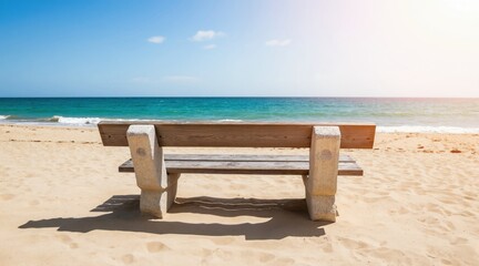 Fototapeta premium Wooden bench on sandy beach faces calm blue ocean waves under clear sky. Warm sunlight illuminates empty seaside. Perfect spot for peaceful relaxation.