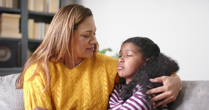 African American mother noticing and holding child in striped top withdrawing on sofa to calm