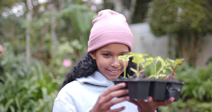 African American teen lifting black seed tray, checking growth in garden as helper hand holding