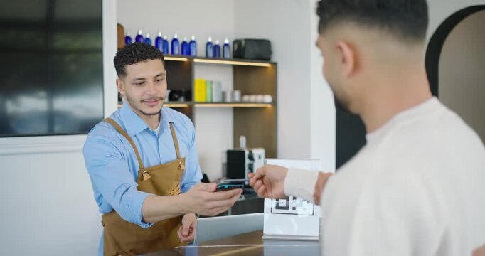 African American male barista seeing card offering reader for payment customer tapping near QR code