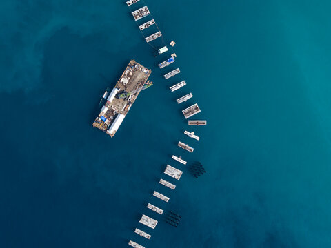 Aerial view of the Oil Fuel Terminal Port featuring a construction barge and concrete pilings extending into the deep blue sea in Manggis, Bali, Indonesia.