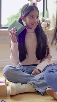 Vertical video: Mom handing gift making girl in antlers shaking, opening gifts by window, guessing