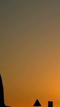 Vertical video: Reaching boys chasing ball overhead, lunging along curb at sunset in sportswear