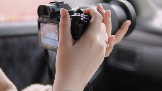 Hands hold camera inside car, preparing to capture view. Fingers steady on grip, lens focused outward. Soft focus on background hints at travel or road trip. Ideal for travel, vlogging