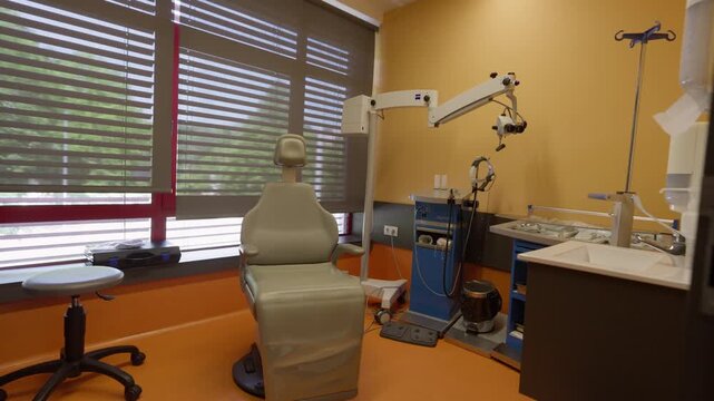 An empty, modern medical examination room equipped with a patient chair and specialized medical instruments, ready for use.