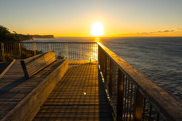 Obraz premium Sunrise over the Pacific Ocean viewed from the Bondi to Coogee Coastal Walk with golden light reflecting across calm water, Sydney, Australia.