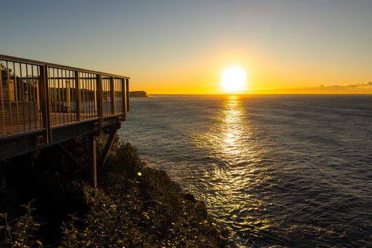 Sunrise over the Pacific Ocean viewed from the Bondi to Coogee Coastal Walk with golden light reflecting across calm water, Sydney, Australia.