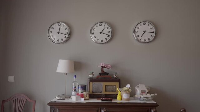 Three round clocks showing different times on a gray wall above a vintage wooden cabinet with various items.