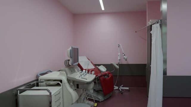 An empty, modern medical examination room with various equipment and a red examination chair, ready for patient care.