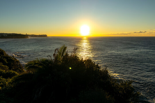Sunrise over the Pacific Ocean viewed from the Bondi to Coogee Coastal Walk with golden light reflecting across calm water, Sydney, Australia.