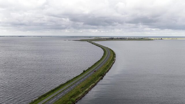Amazing aerial view of a car driving along the curving causeway, a long dam markermeer lakes in the netherlands under a cloudy sky