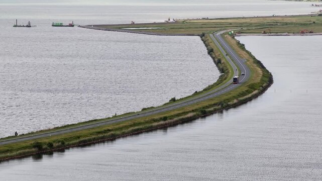 Elevated view of vehicles, including cars and trucks, traveling along scenic causeway, a long dike road stretching across the water in the netherlands