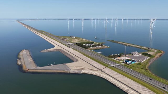 Impressive aerial perspective showing the afsluitdijk, a major causeway in the netherlands, with traffic moving along the highway and a large offshore wind farm generating clean energy
