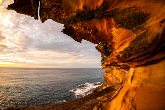 Sunrise illuminates sculpted sandstone cliffs and coastal rock formations overlooking the Pacific Ocean along the Sydney coastline, New South Wales, Australia.