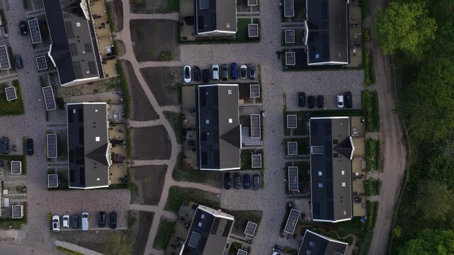 Top down aerial view slowly moving over a modern dutch residential area featuring newly built houses with dark roofs, solar panels, and gardens under construction in a suburban district