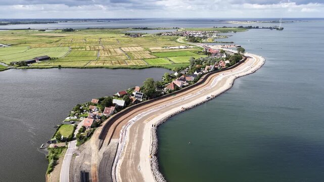 Extensive flood defense construction along a coastal village with a newly built dike providing protection against rising sea levels, showcasing climate change adaptation and land reclamation