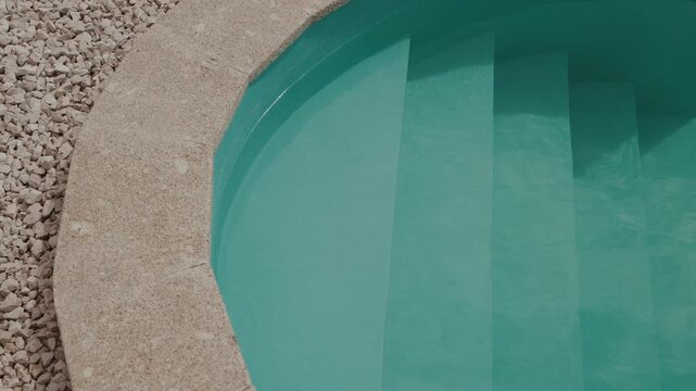 Curved swimming pool steps and stone coping beside gravel landscaping closeup detail