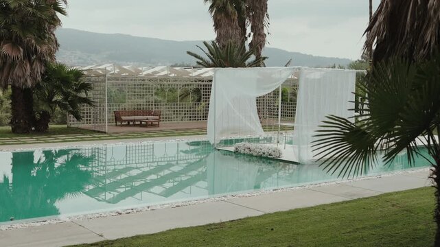 White draped wedding canopy over pool with floral platform lattice pergola palms and mountain view
