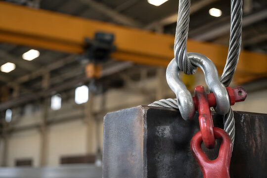 Industrial Rigging Equipment Steel Wire Sling Shackle and Hook Connected to Heavy Metal Load in Warehouse with Overhead Crane Structure in Background Lifting Safety Equipment