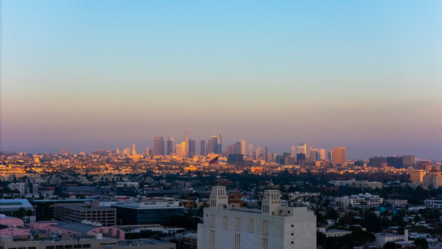 Aerial view of the Los Angeles skyline at sunset with warm golden light illuminating the skyscrapers and urban sprawl in Los Angeles, California, United States.