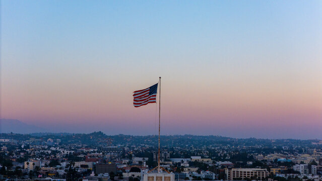 Aerial view of an American flag waving on a pole above the urban sprawl of Los Angeles at dusk, Los Angeles, California, United States.