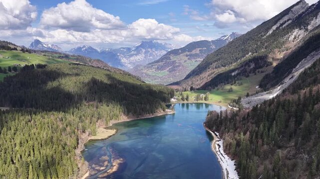 Cinematic drone push toward Obersee lake surrounded by forests, alpine slopes and dramatic Swiss mountains near N&auml;fels, Glarus.